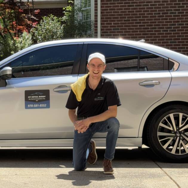 Samuel Zimmerman smiling in front of a silver car, wearing his My Detail Buddy shirt